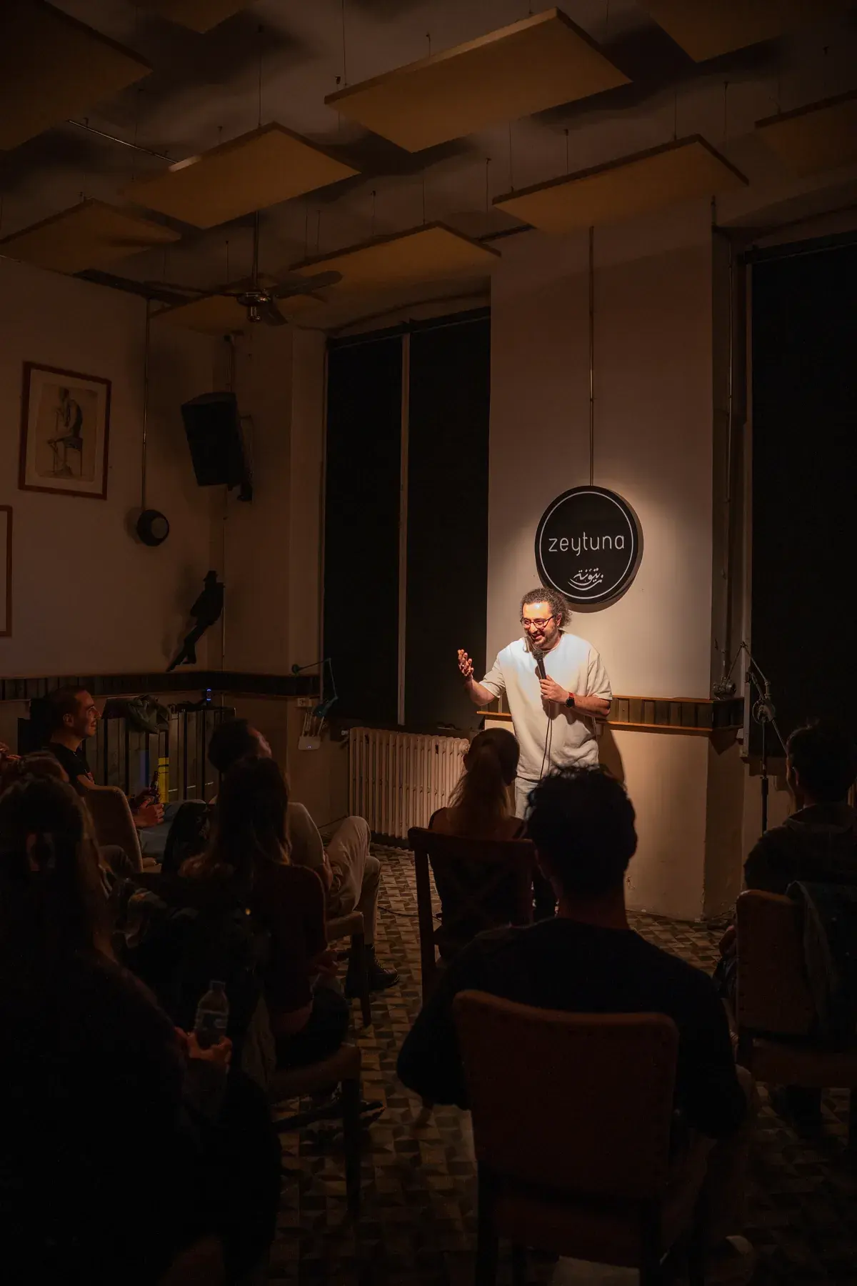 The room at Zeytuna during a show, seen from the back: the audience watching a comedian in the spotlight